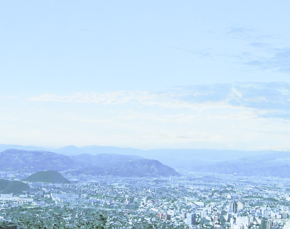 青空の下に広がる市街地と山並み